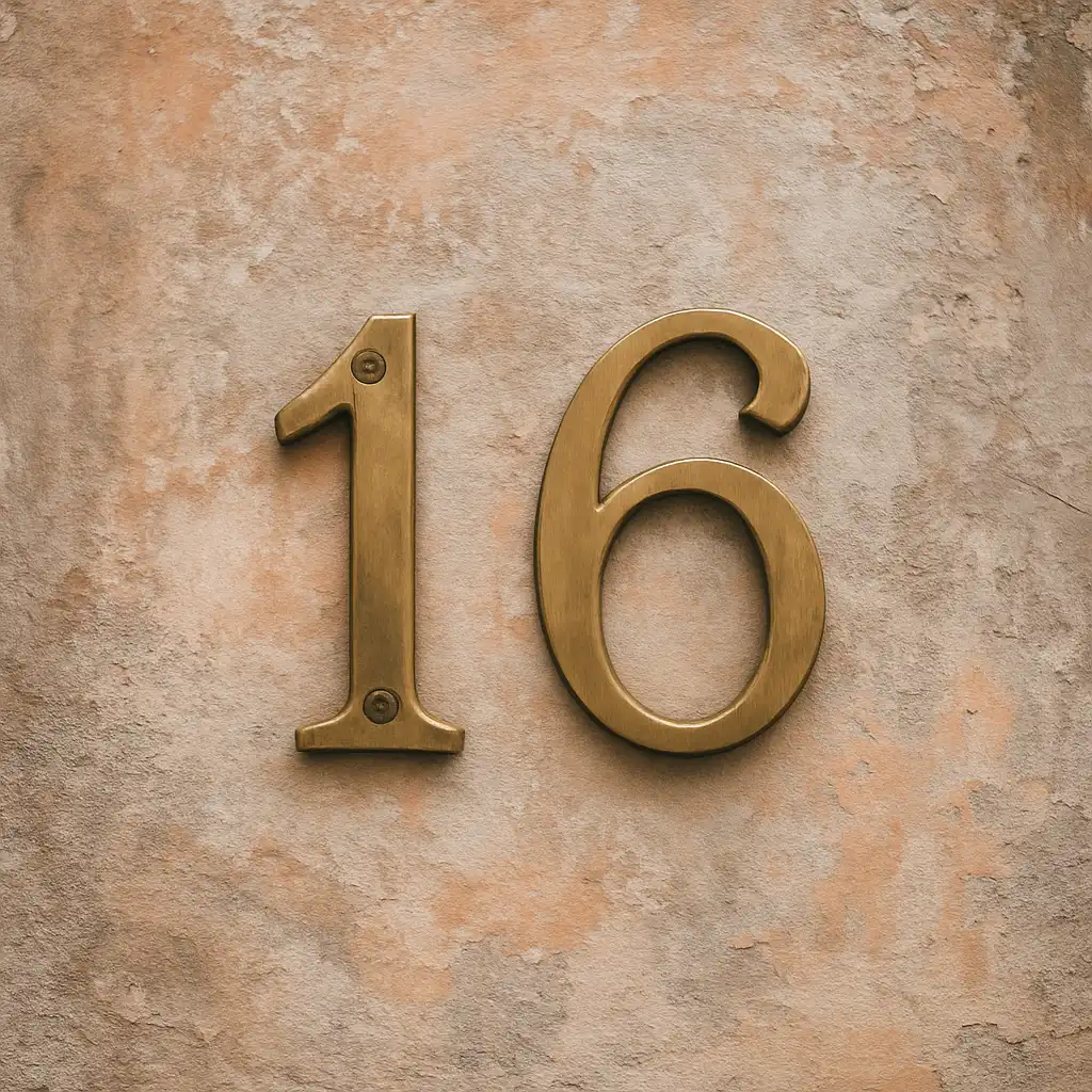 A photograph captures the number 16 displayed on a textured wall in metallic brass numerals, softly lit to highlight its warm tone and vintage surface.
